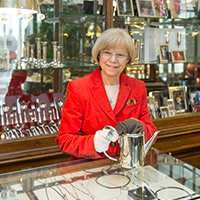 Blonde Frau mit roter Jacke in einem Juweliergeschäft beim Reinigen einer Silberkanne